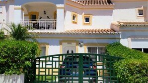 A two-story building with a white facade, yellow trim, and a green gate.