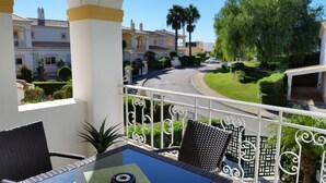 A balcony with wicker furniture, a view of a street, and a building with a tiled roof.