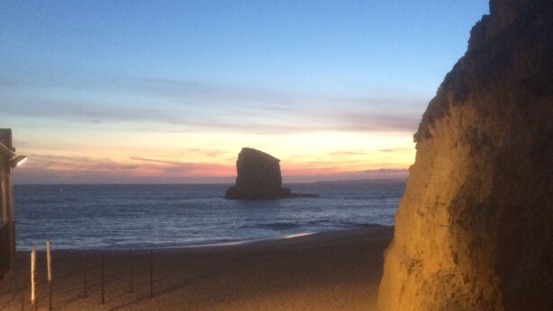 A beach with a rock formation, a wooden bench, and a fence.