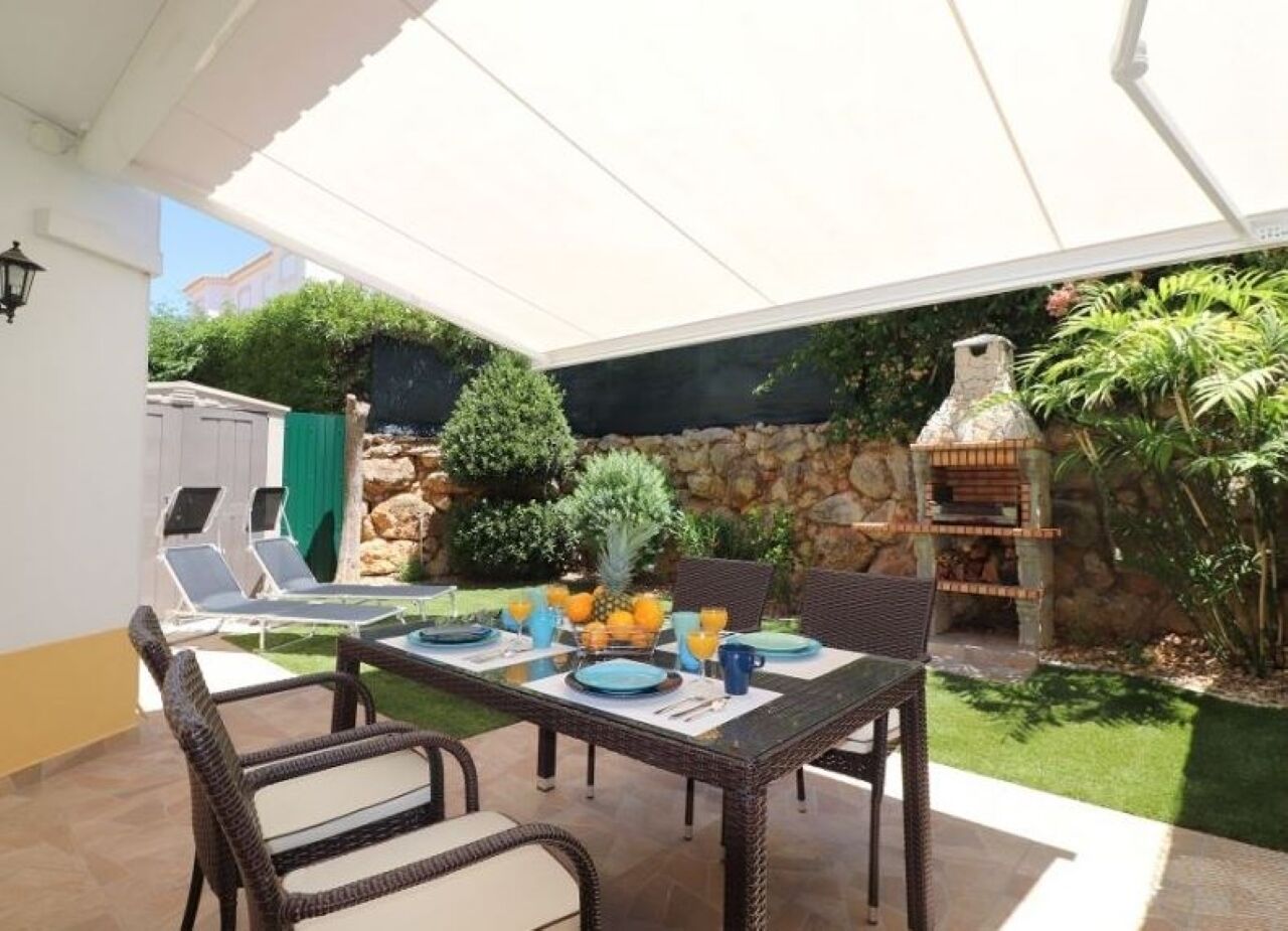 An outdoor patio with a table set for dining, wicker chairs, a stone wall, and a barbecue grill.