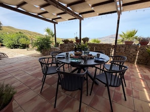 A covered patio with a round table and chairs, surrounded by potted plants and a stone wall. - Villa di Pietro – Historic/newly renovated stone villa with a pool and ocean view! (Sicilia)