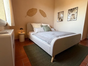 Ein Schlafzimmer mit einem Bett, einem Nachttisch, einer Lampe, einem Heizkörper und zwei an der Wand befestigten Kunstwerken.