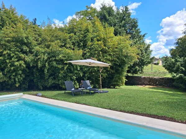 A swimming pool with two lounge chairs and an umbrella, surrounded by lush greenery and a stone wall. - Bed and Breakfast 'La Chambre Du Rouge-gorge' with Shared Pool, Private Terrace and Wi-Fi (Moissannes)