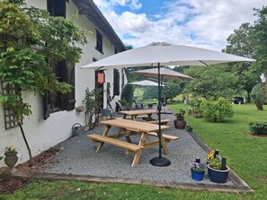 A patio with wooden tables and benches, surrounded by gravel, potted plants, and a white building with black shutters. - Bed and Breakfast 'La Chambre Du Rouge-gorge' with Shared Pool, Private Terrace and Wi-Fi (Moissannes)