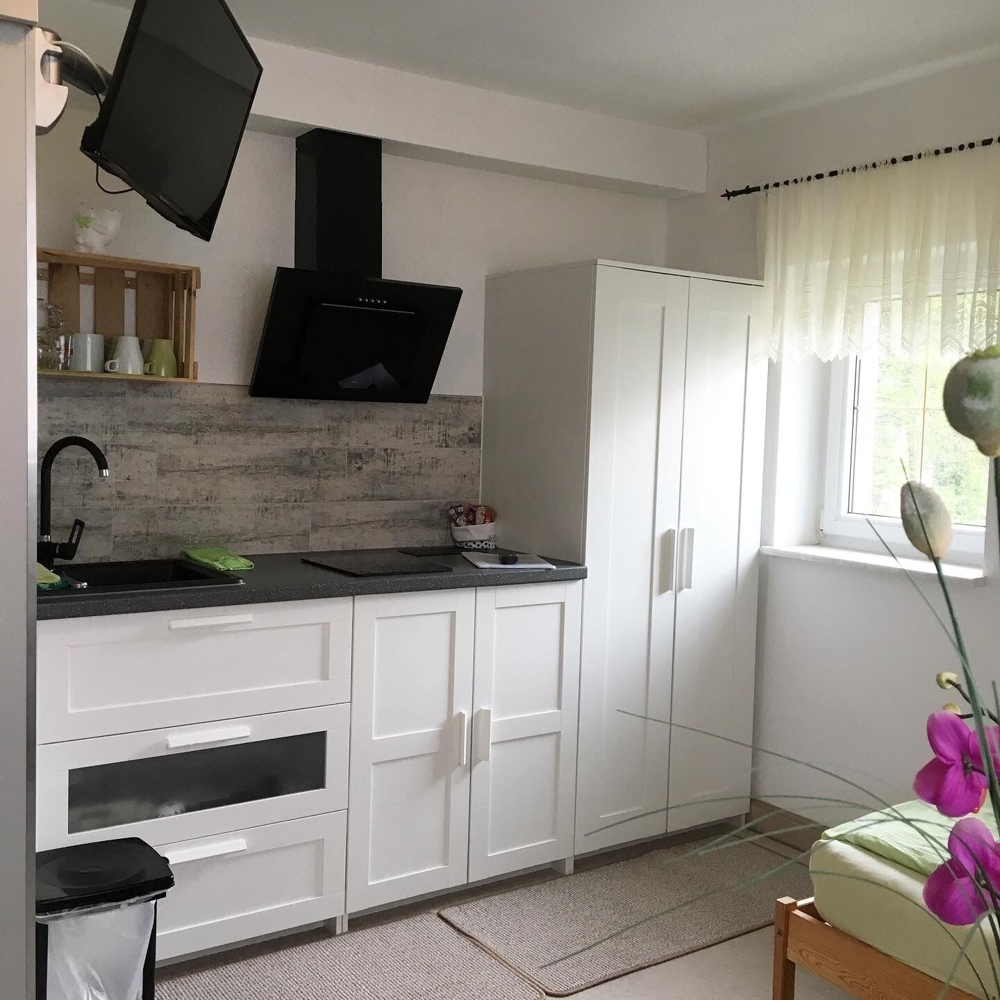 A compact kitchen with white cabinets, a black range hood, a sink, and a window with a view of greenery.