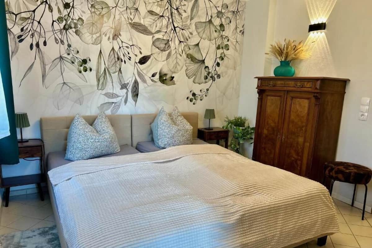 A bedroom with a large bed, a wall tapestry, a wooden cabinet, and a lamp.