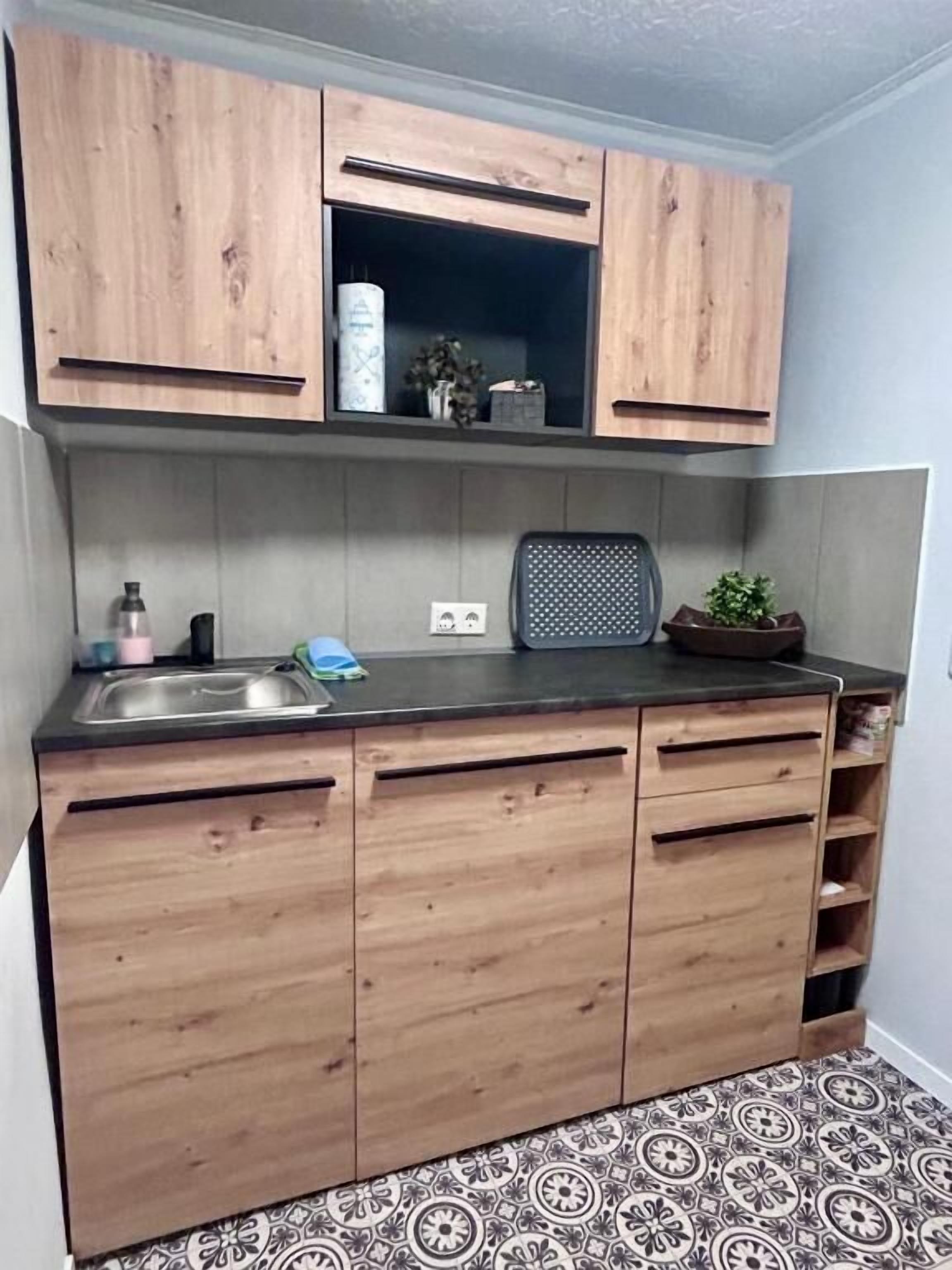 A kitchen with wooden cabinets, a black countertop, and patterned floor tiles.