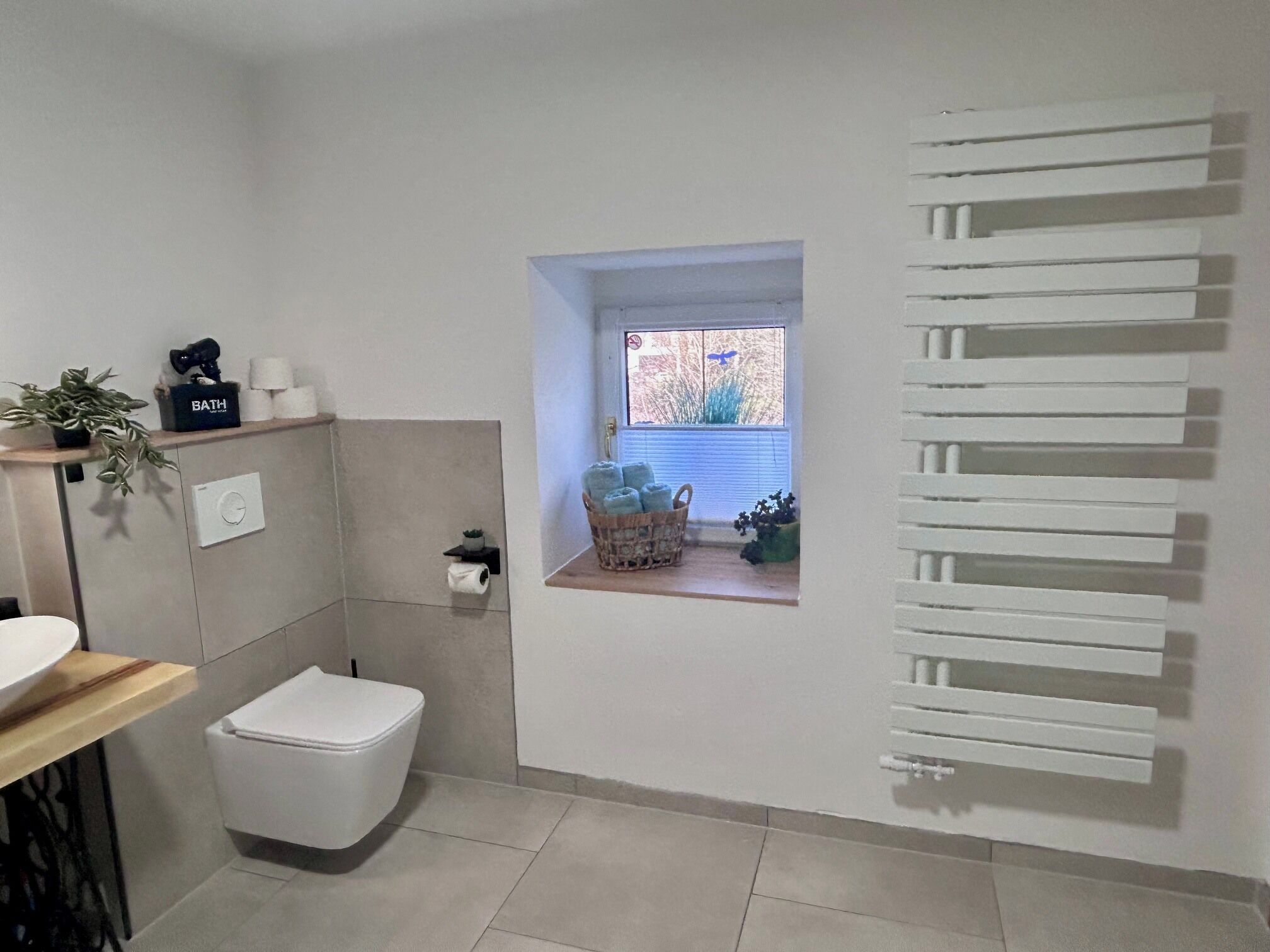 A bathroom with a toilet, a shelf with toiletries, a small window, and a towel rack.