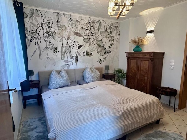 Un dormitorio con una cama grande, un mural en la pared, un armario de madera y una araña.