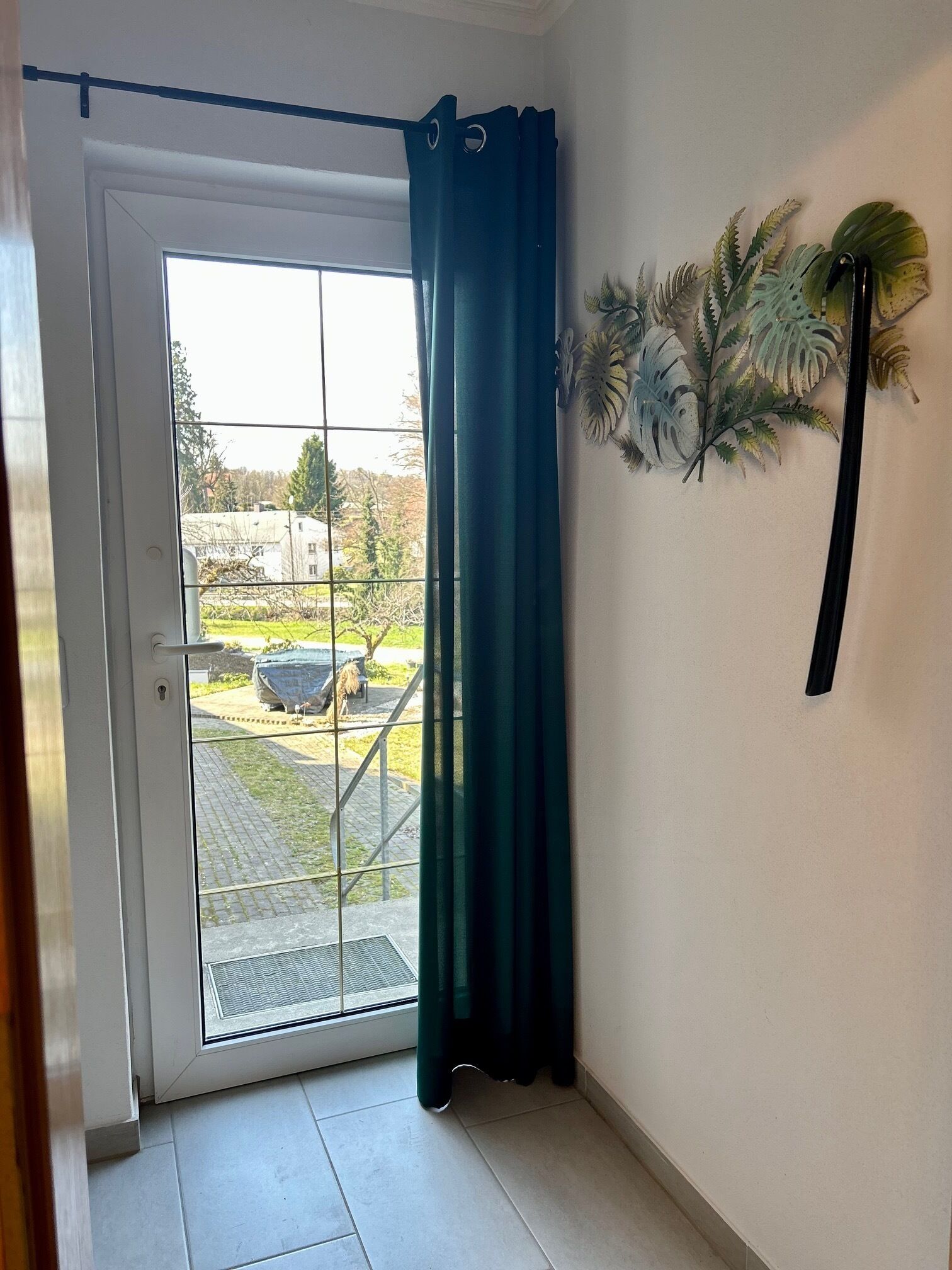 Una habitación con puerta corrediza de vidrio, cortina verde y planta en la pared.