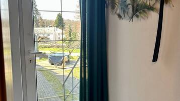 Una habitación con puerta corrediza de vidrio, cortina verde y planta en la pared.