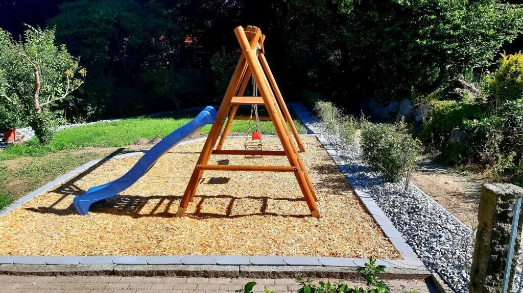 A playground with a wooden swing set and a blue slide.