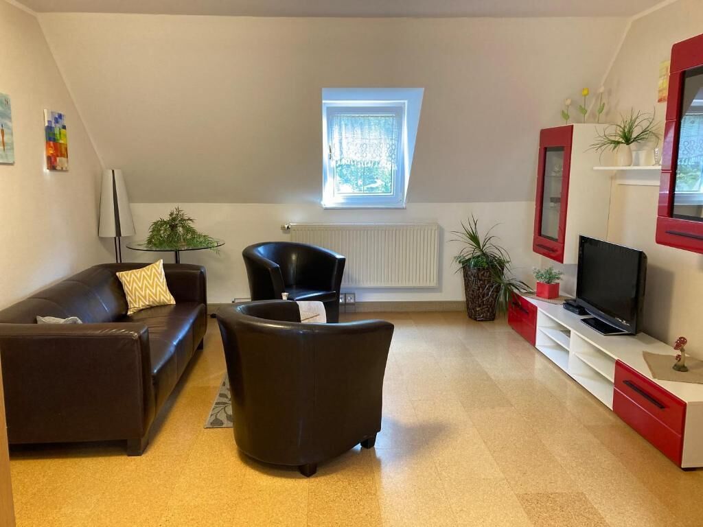 A living room with a sofa, armchair, TV, and a small table with a plant.