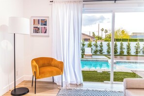 A modern living room with a sofa, a floor lamp, a chair, a large window with a view of a swimming pool and a garden. - Marvelous 5-bedroom house with pool (Palm Springs)