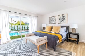Ein Schlafzimmer mit Bett, Nachttischen, einer Bank und Blick auf einen Pool sowie zwei Wandbildern.