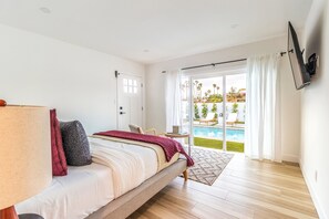 Ein Schlafzimmer mit Bett, Fernseher, einer Tür und Blick auf einen Swimmingpool.