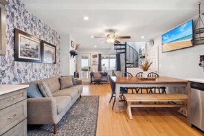 A modern living room with a sofa, coffee table, and dining table. There is a staircase leading to an upper level. - Beachfront Bliss | AC | On the Beach | Sunrises (Salisbury)