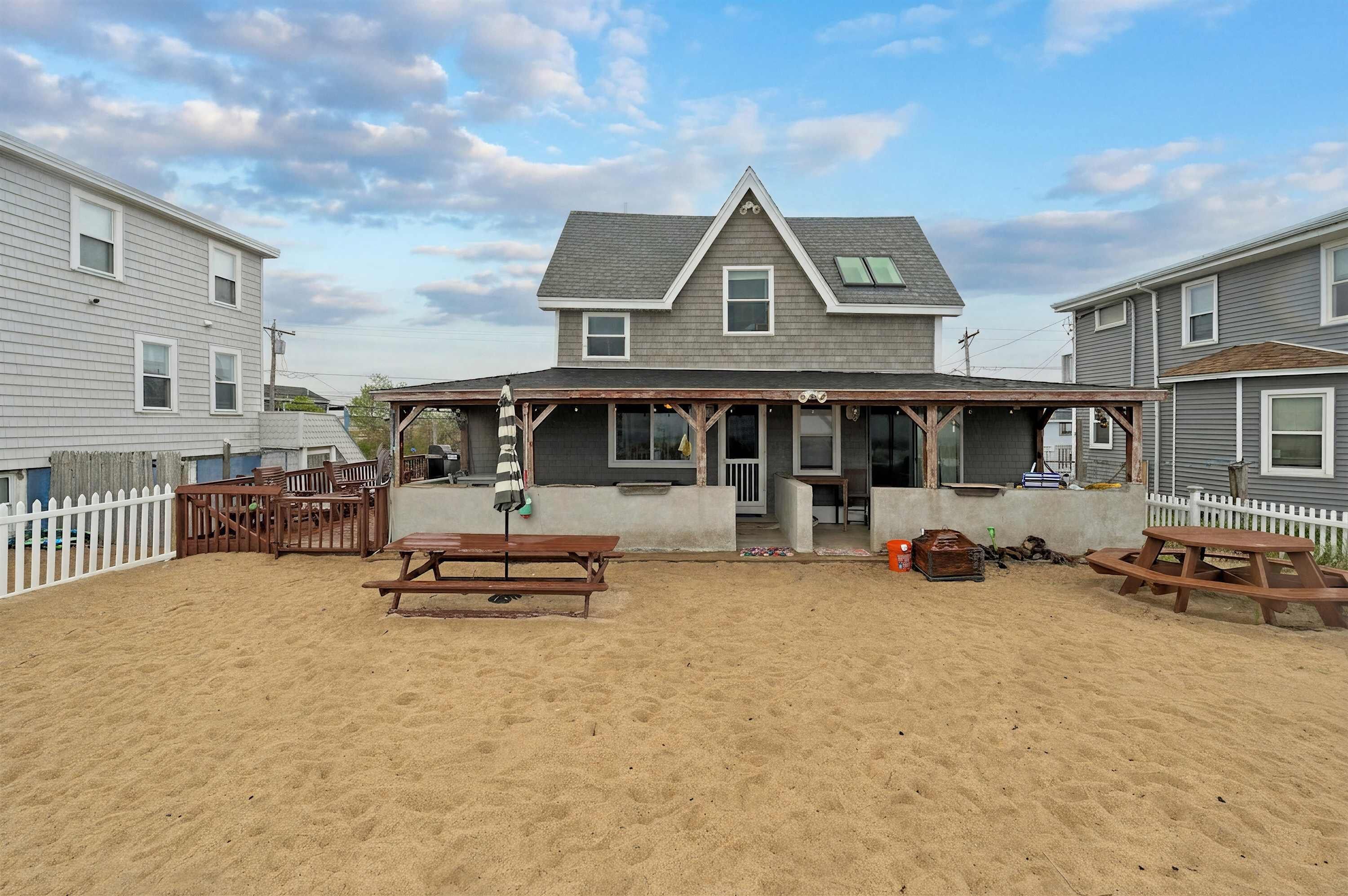 A beach house with a covered patio, picnic tables, and a white picket fence.