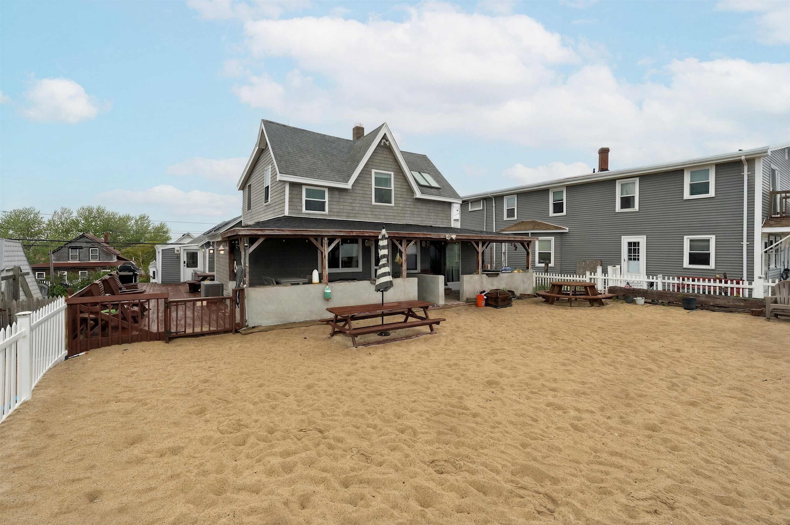 A beach house with a covered patio, a wooden deck, and a sandy yard.
