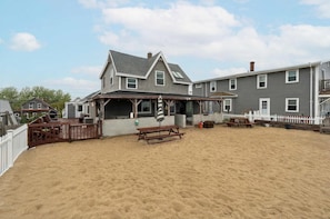 A beach house with a covered patio, a wooden deck, and a sandy yard. - Beachfront Bliss | AC | On the Beach | Sunrises (Salisbury)