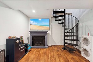 Ein Zimmer mit Kamin, darüber ein montierter Fernseher, eine Wendeltreppe und eine Waschmaschine.