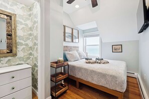 Une chambre à coucher avec un lit, une commode, une étagère en bois et une fenêtre donnant sur un beau paysage.