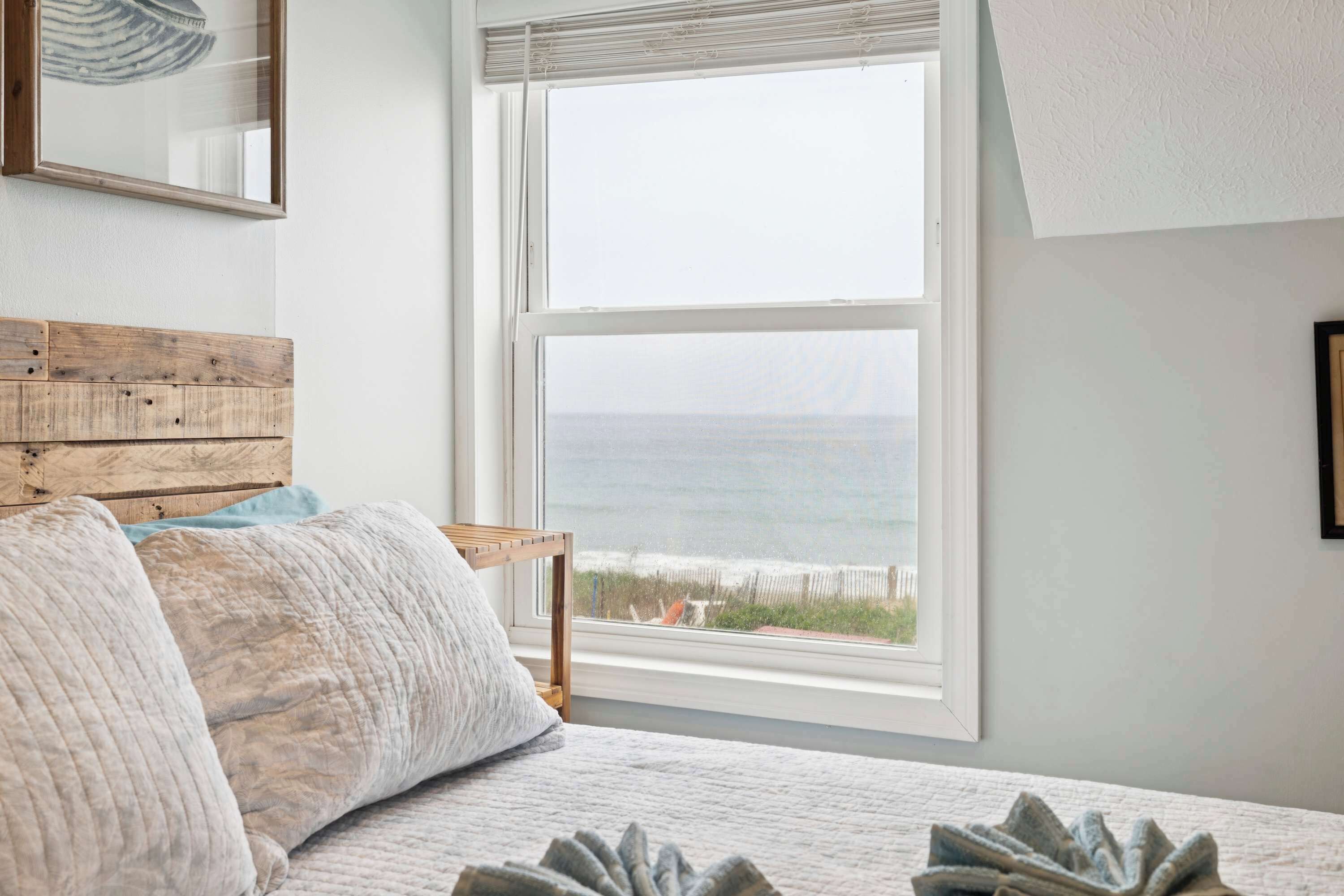 A bedroom with a large window, a wooden headboard, and a view of the sea.