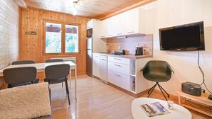 A compact kitchen with white cabinets, a microwave, and a flat-screen TV mounted on the wall.