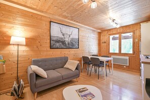 Tunnelmallinen huone, jossa on harmaa sohva, ruokapöytä tuoleineen, seinällä oleva taulu ja ikkuna, josta avautuu näkymä puihin.