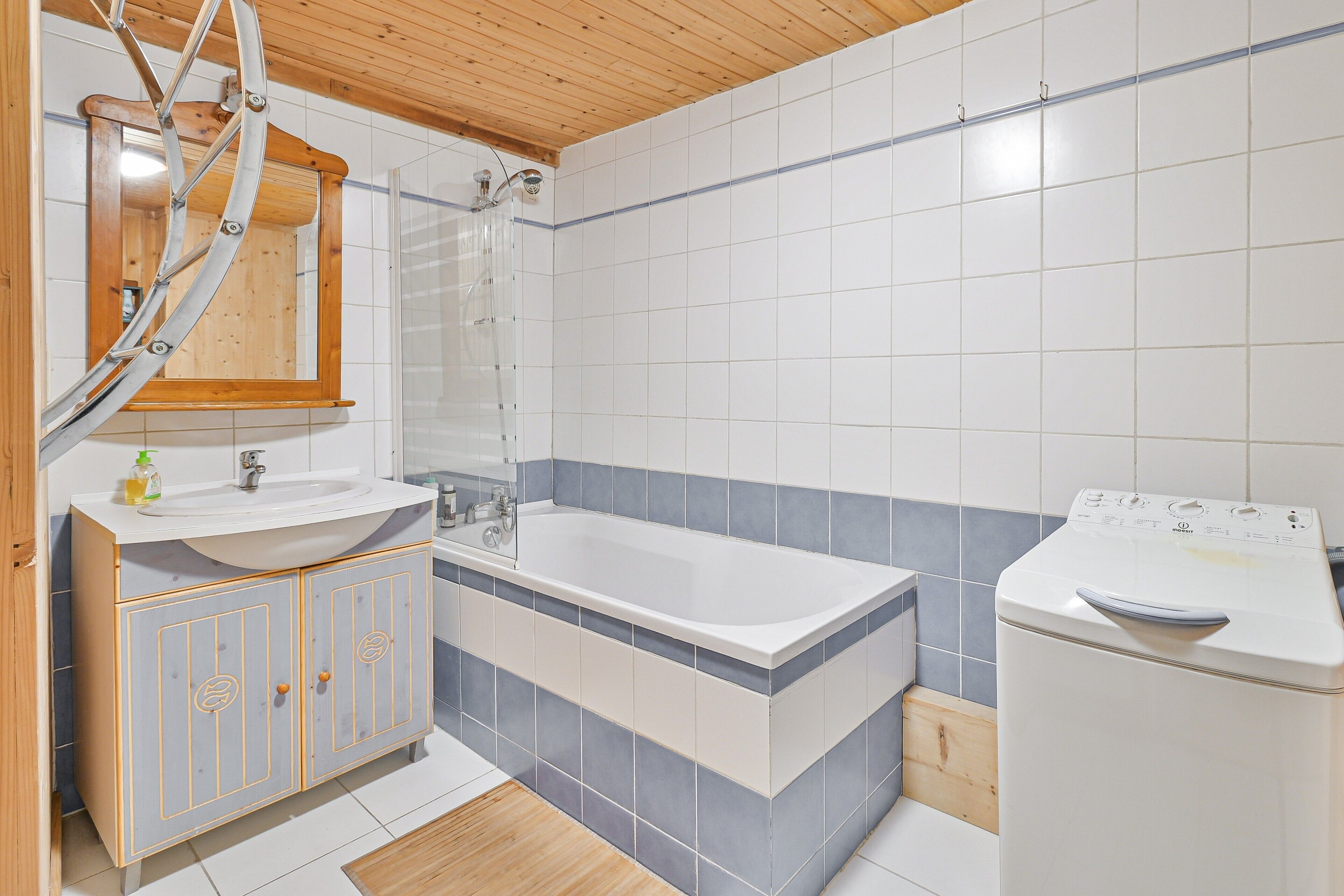 Une salle de bain avec un plafond en bois, un lavabo blanc avec un miroir au-dessus, une baignoire et un lave-linge.