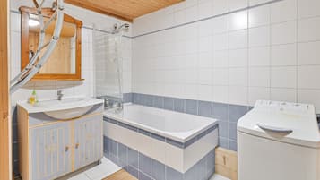 Une salle de bain avec un plafond en bois, un lavabo blanc avec un miroir au-dessus, une baignoire et un lave-linge.