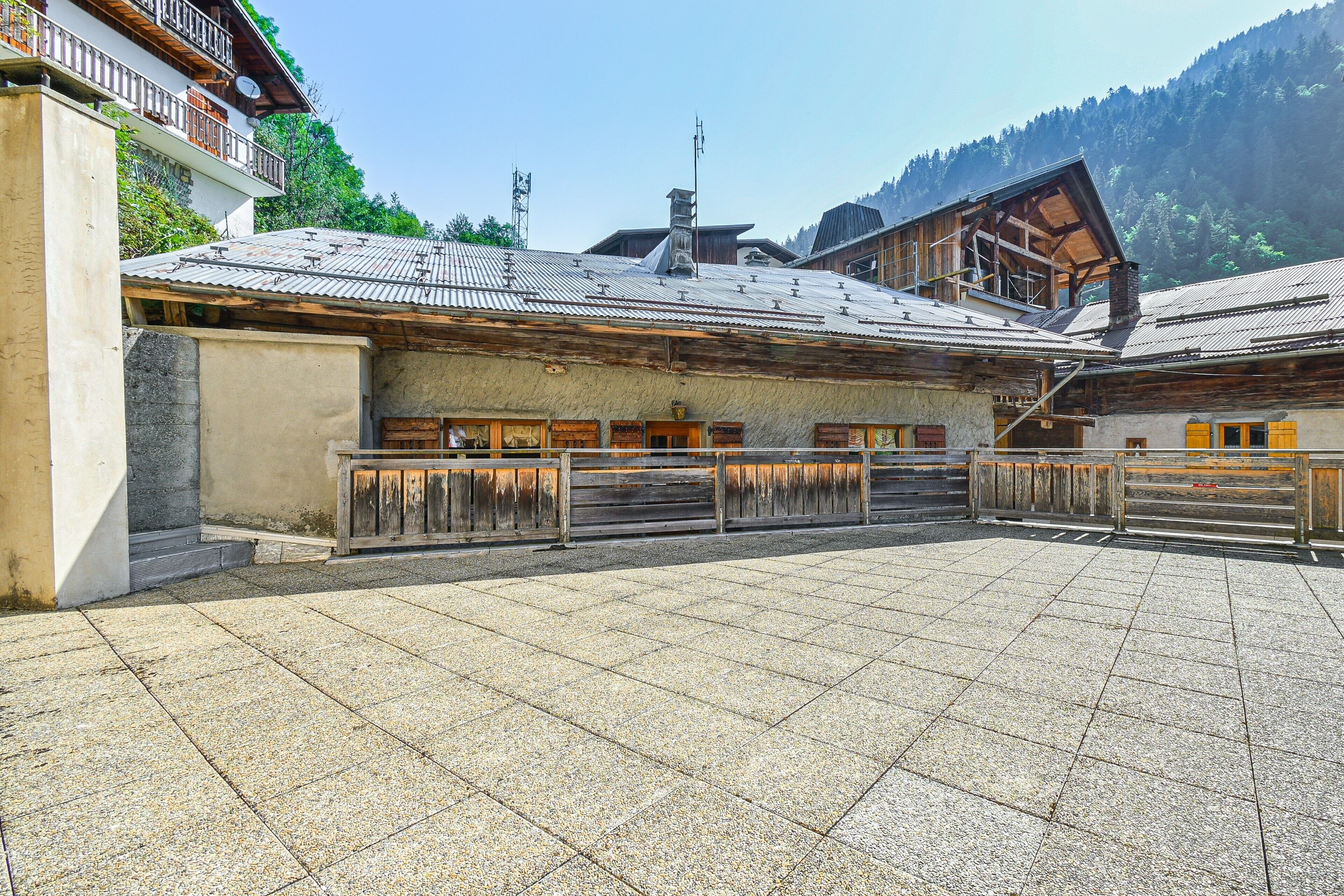 Une cour dallée de pierres, avec des bancs en bois et des bâtiments traditionnels en bois surmontés de toits en métal.