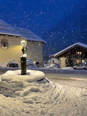 Une rue enneigée, de nuit, avec un lampadaire et des bâtiments en arrière-plan.