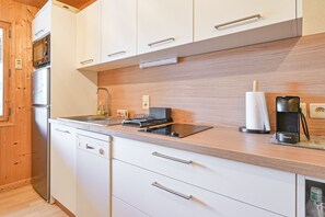 Uma cozinha moderna com armários brancos, uma geladeira de aço inoxidável, máquina de lavar louça embutida e bancada de madeira.