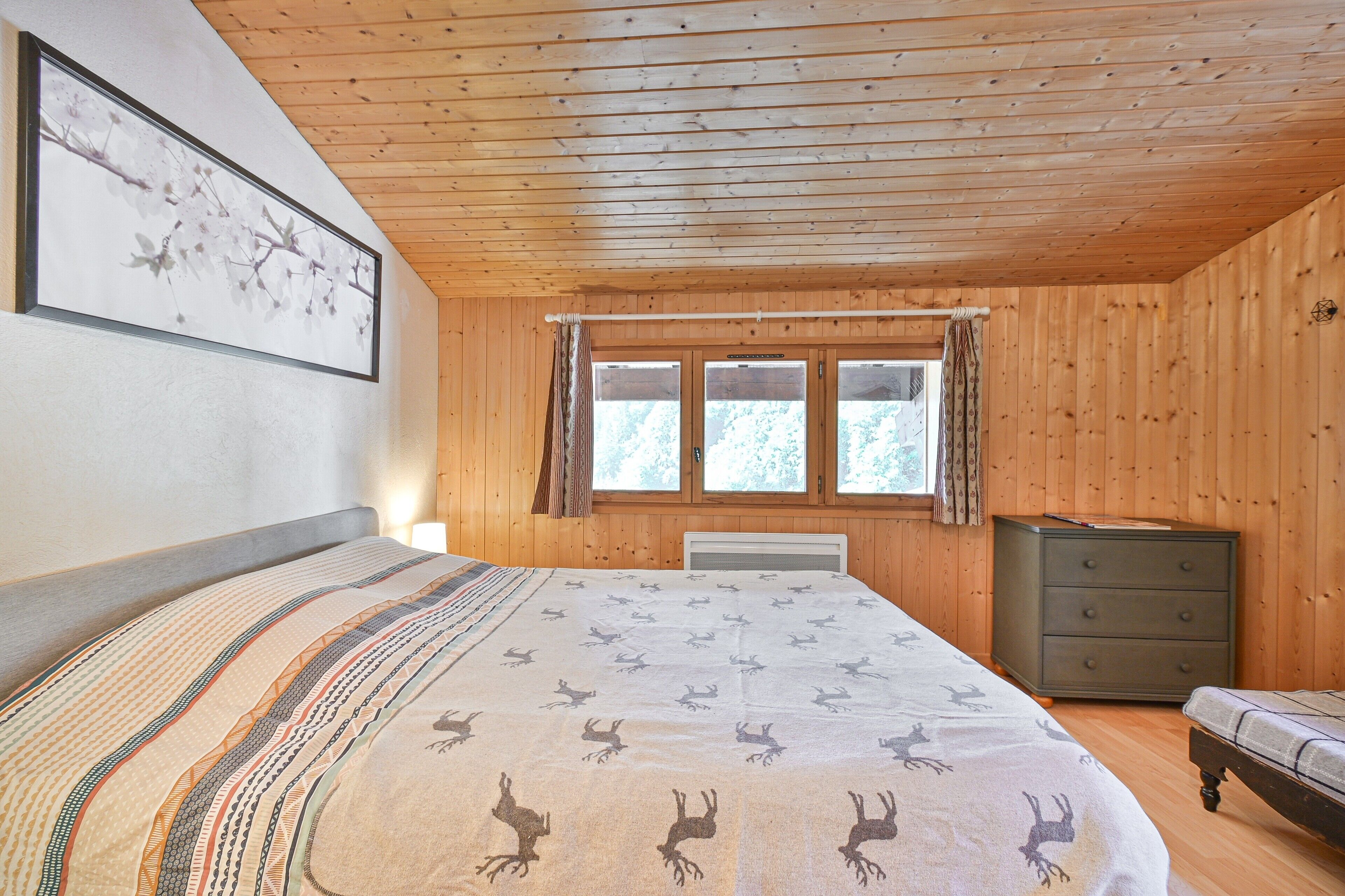 Een slaapkamer met een bed, een dressoir, een raam en een ingelijst schilderij aan de muur.