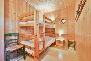 Huoneessa on puinen kerrossänky, tuoli ja pieni pöytä.