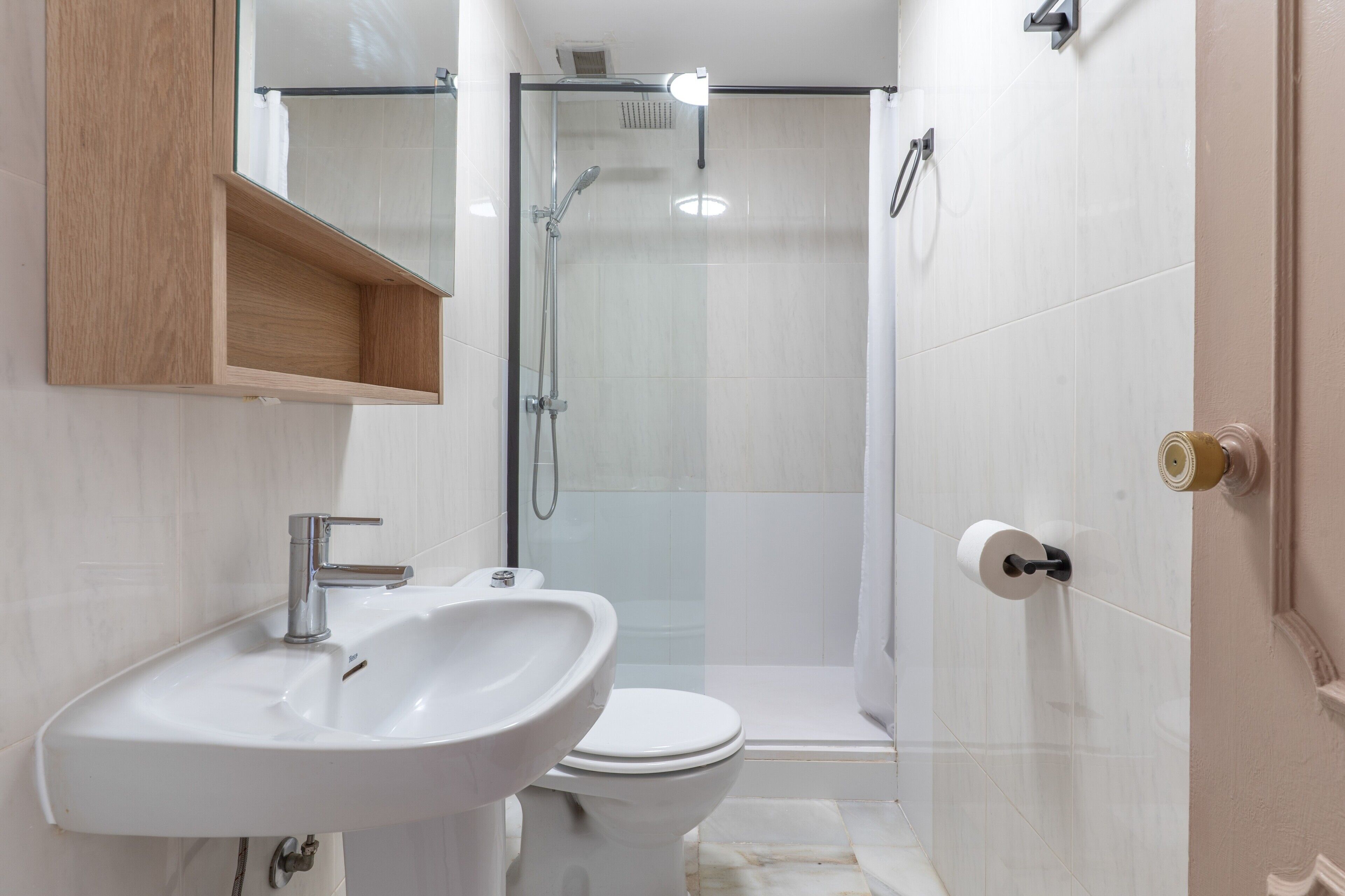 A bathroom with a sink, toilet, shower, and a wooden medicine cabinet.