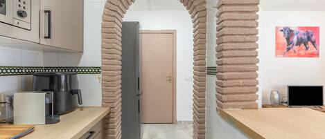 Una cocina con un arco de ladrillo, un refrigerador, una cafetera y un cuadro en la pared.