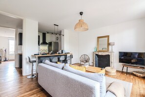 A modern living room with a sofa, a coffee table, a TV, a fireplace, and a kitchen area with a dining table. - Le Jeanne d’Arc – City center & sleeps 8 (Reims)