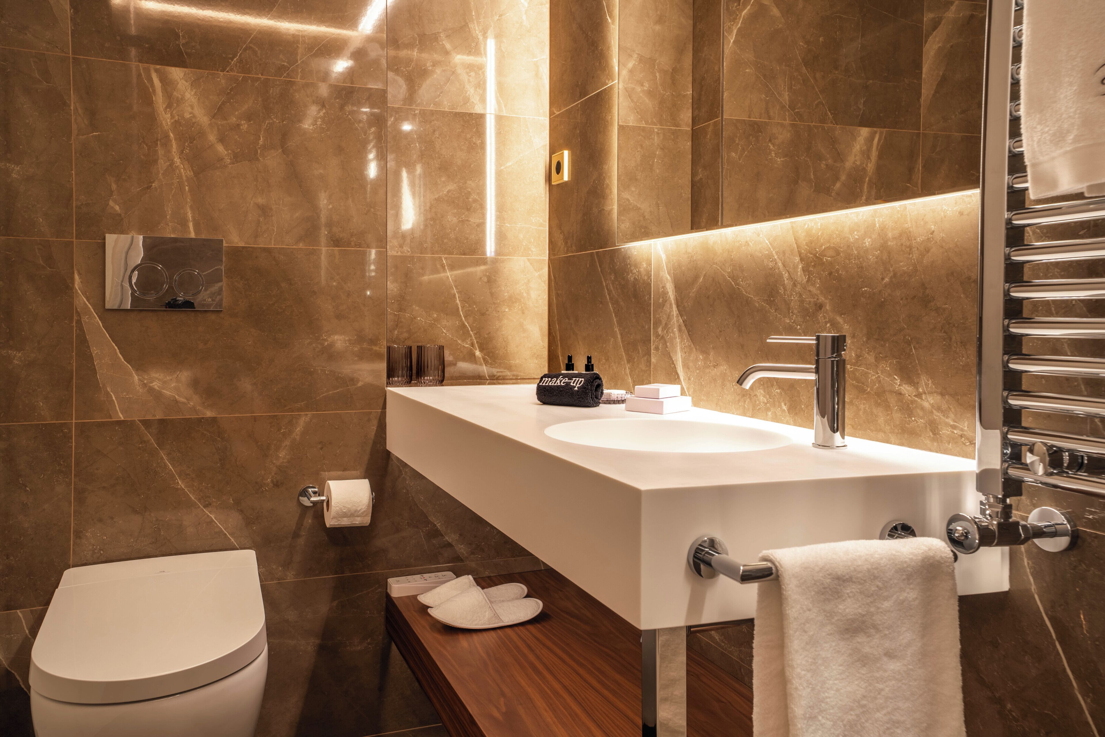 A modern bathroom with a white sink, a mirror, a towel rack, and a toilet.