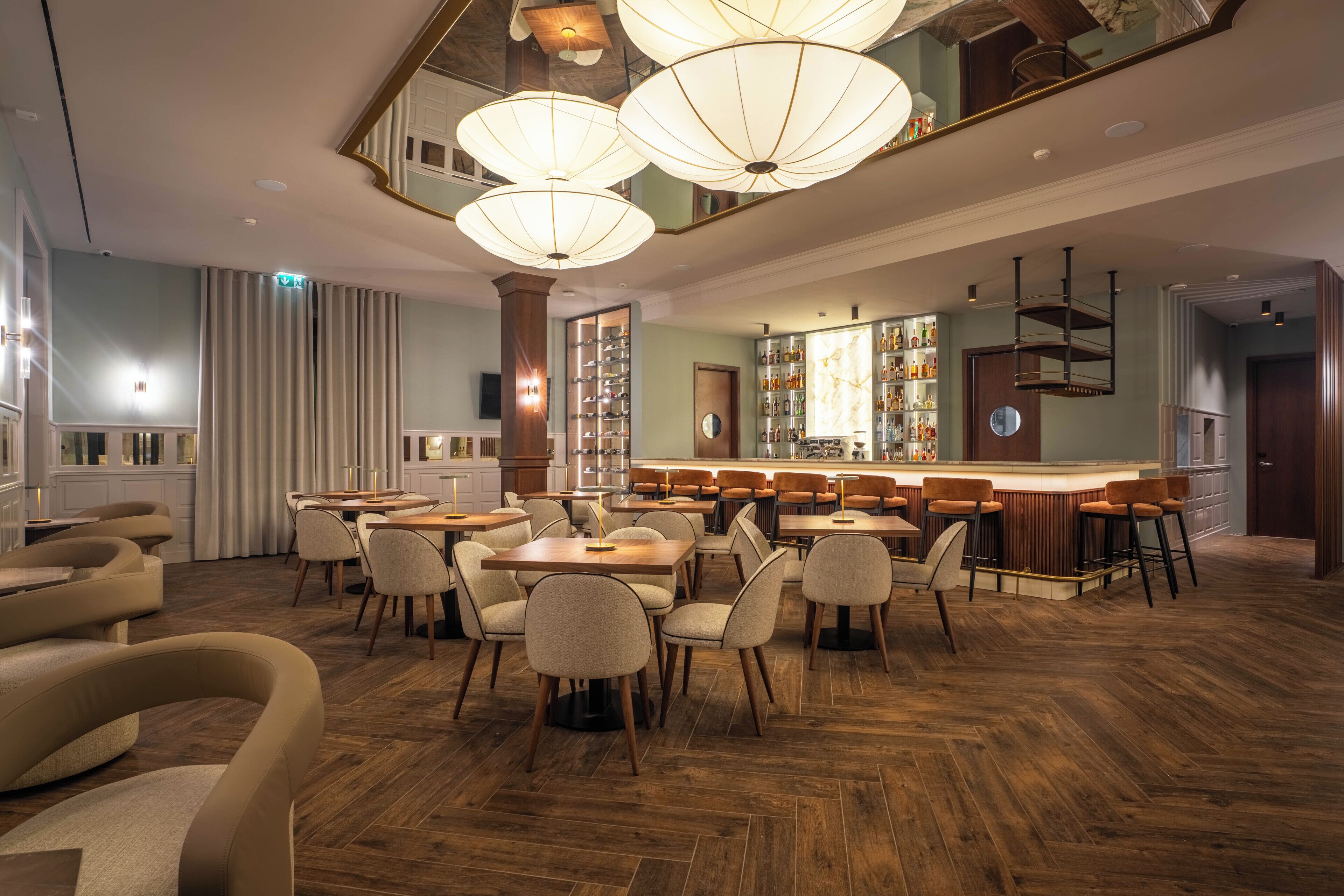 A restaurant with wooden flooring, multiple tables and chairs, and hanging pendant lights.