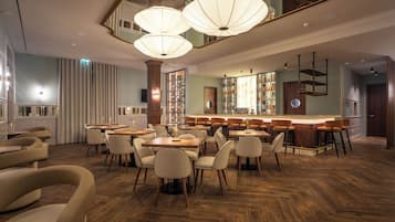 A restaurant with wooden flooring, multiple tables and chairs, and hanging pendant lights.