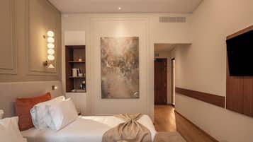 A hotel room with a bed, bedside table, lamp, artwork, and a TV.