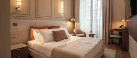 A hotel room with a large bed, bedside tables, a desk with a chair, a TV, and wall-mounted lighting.