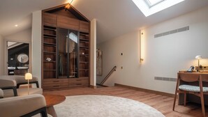 A modern living room with a skylight, wooden shelving, a round coffee table, and a desk with a chair. - The Book Hotel (Horta)