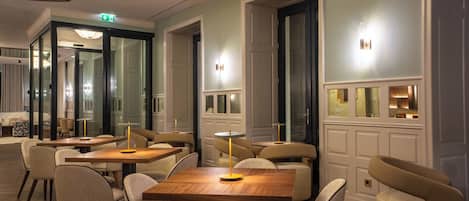 Een moderne hotellobby met houten tafels en stoelen, een glazen scheiding en een trap.