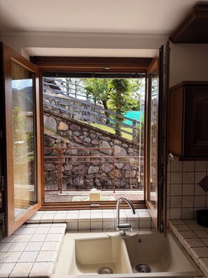 Eine Küche mit einem großen Fenster, einer Spüle und Blick auf eine Steinsäule und Grünfläche.