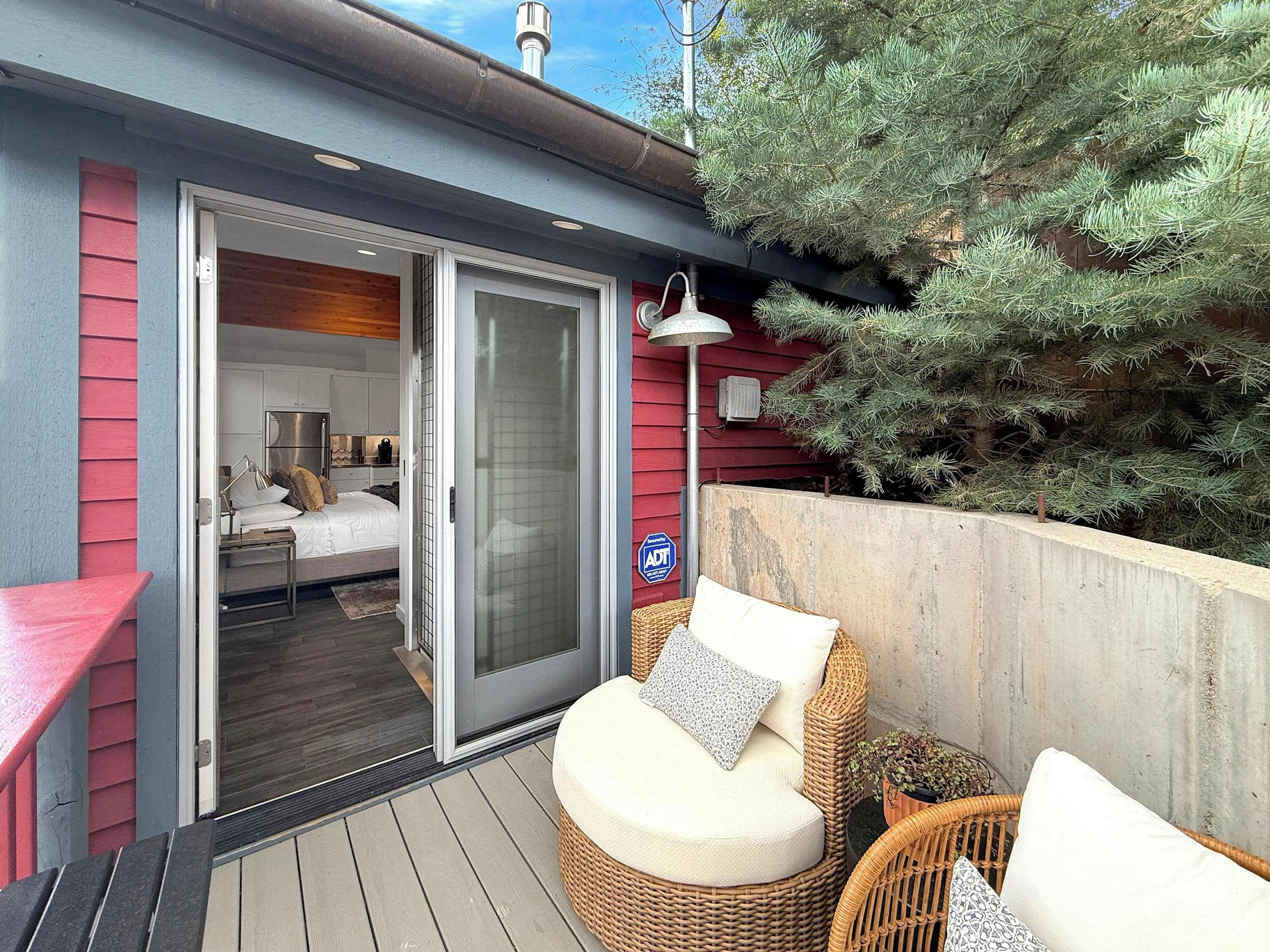A room with a bed, a small table, and a wicker chair on a wooden deck.