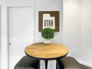 A round wooden table with a potted plant in the center, a framed sign with the word 'UTAH' on the wall, and a door to the left. - Lovebirds paradise by Main Street (Park City)