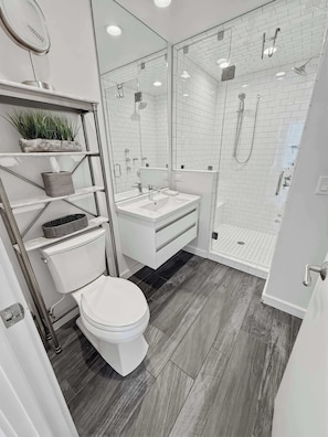Un baño moderno con inodoro, lavamanos y ducha con mampara de vidrio.